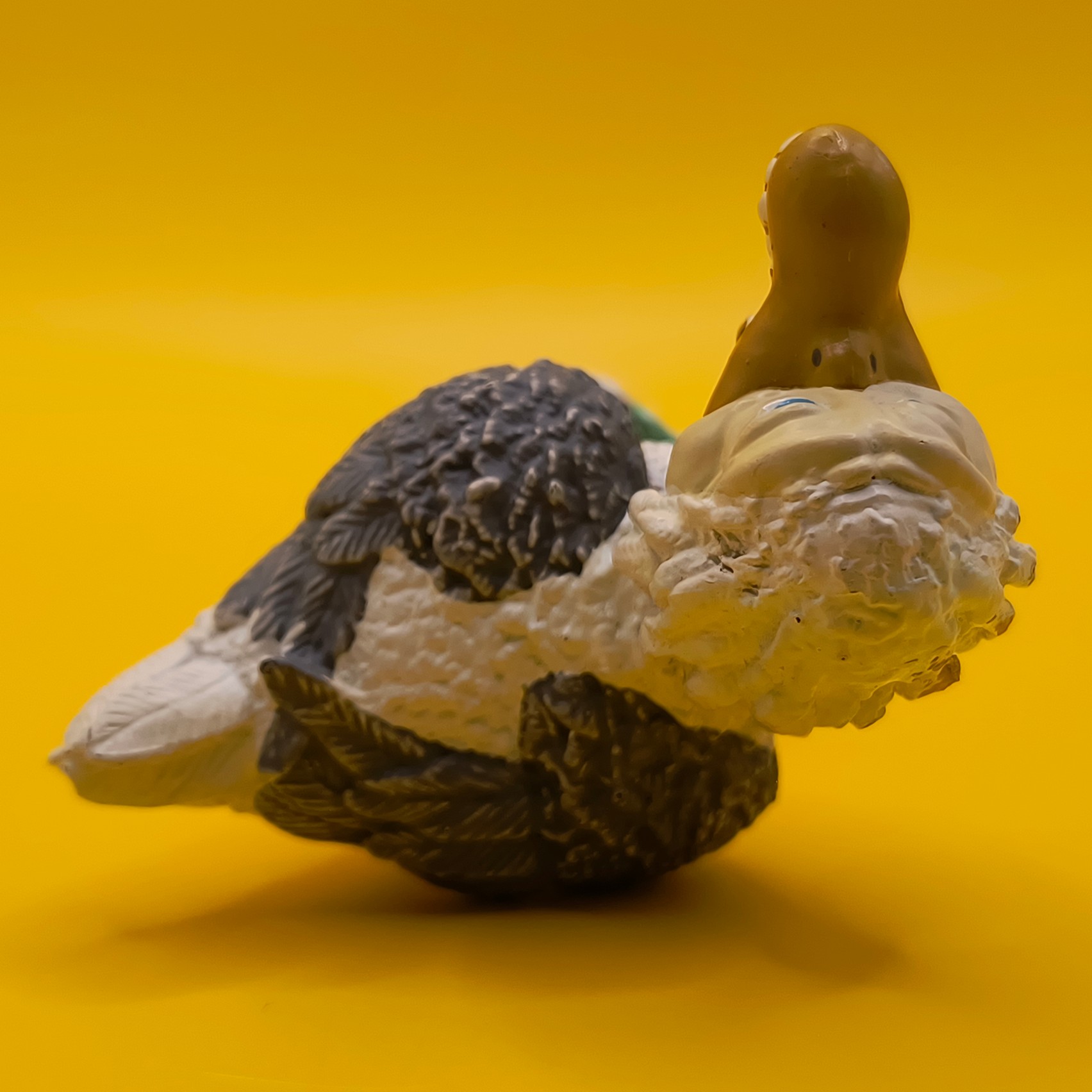 Bøje-figuren fotograferet liggende på siden, set fra en vinkel der viser halsen, det gule næb oppefra samt afskalning på baghovedet.